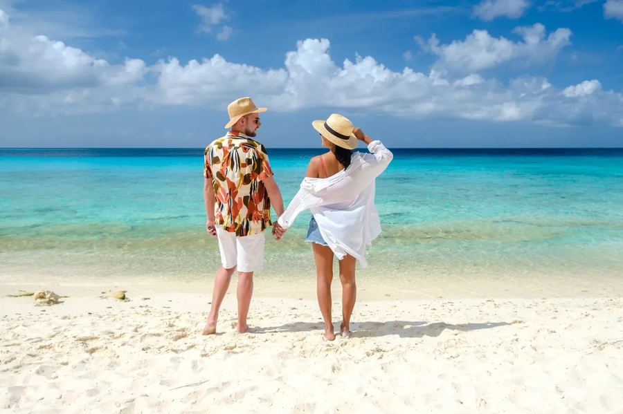 A couple walking along a white-sand beach into turquoise water
